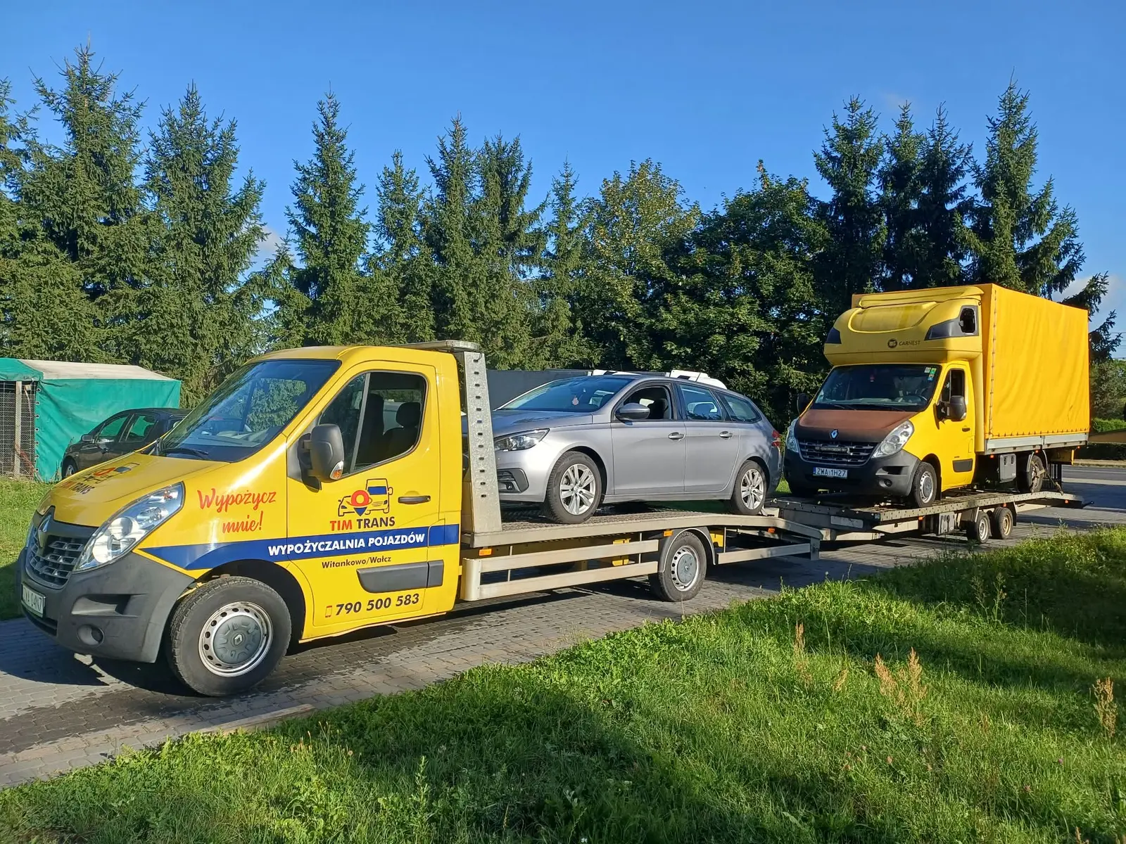 Żółta autolaweta Tim Trans przewożąca samochód osobowy i pojazd dostawczy